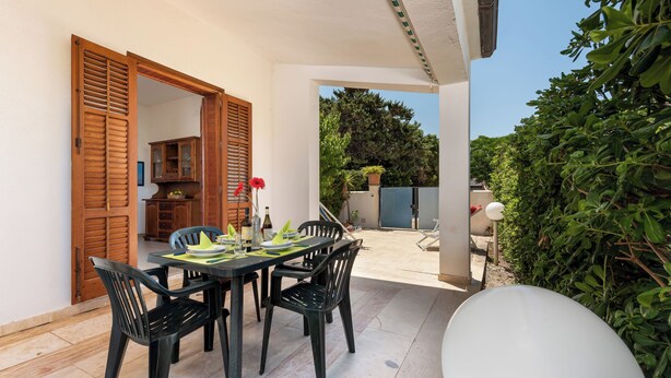 Un patio con una mesa y sillas de comedor, una antena parabólica blanca y una puerta de madera que da a una cocina.