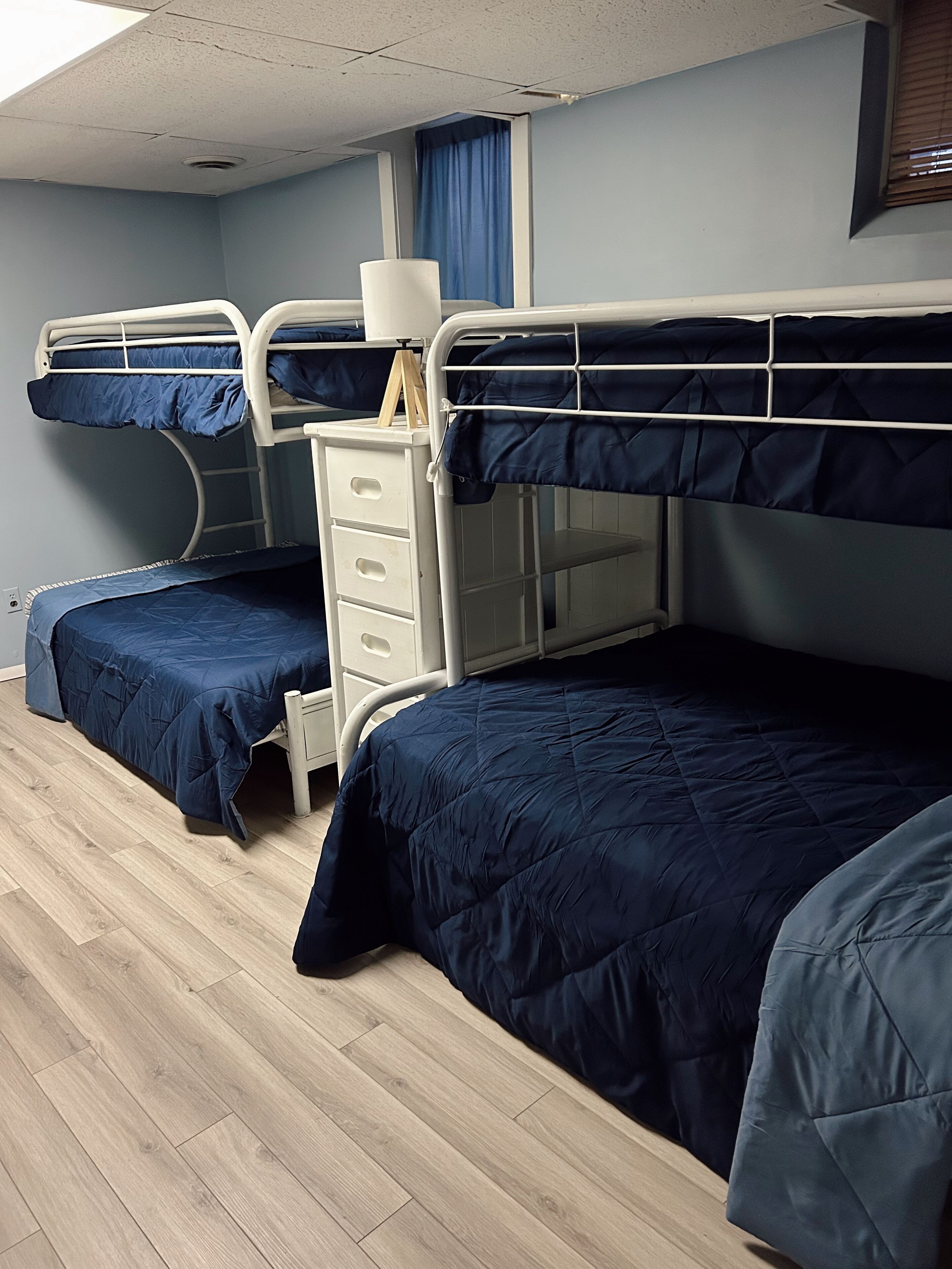 A room with bunk beds, a white dresser, and a window with blue curtains.