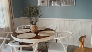 Un coin repas avec une table ronde, des chaises blanches et un vase décoré de branches.