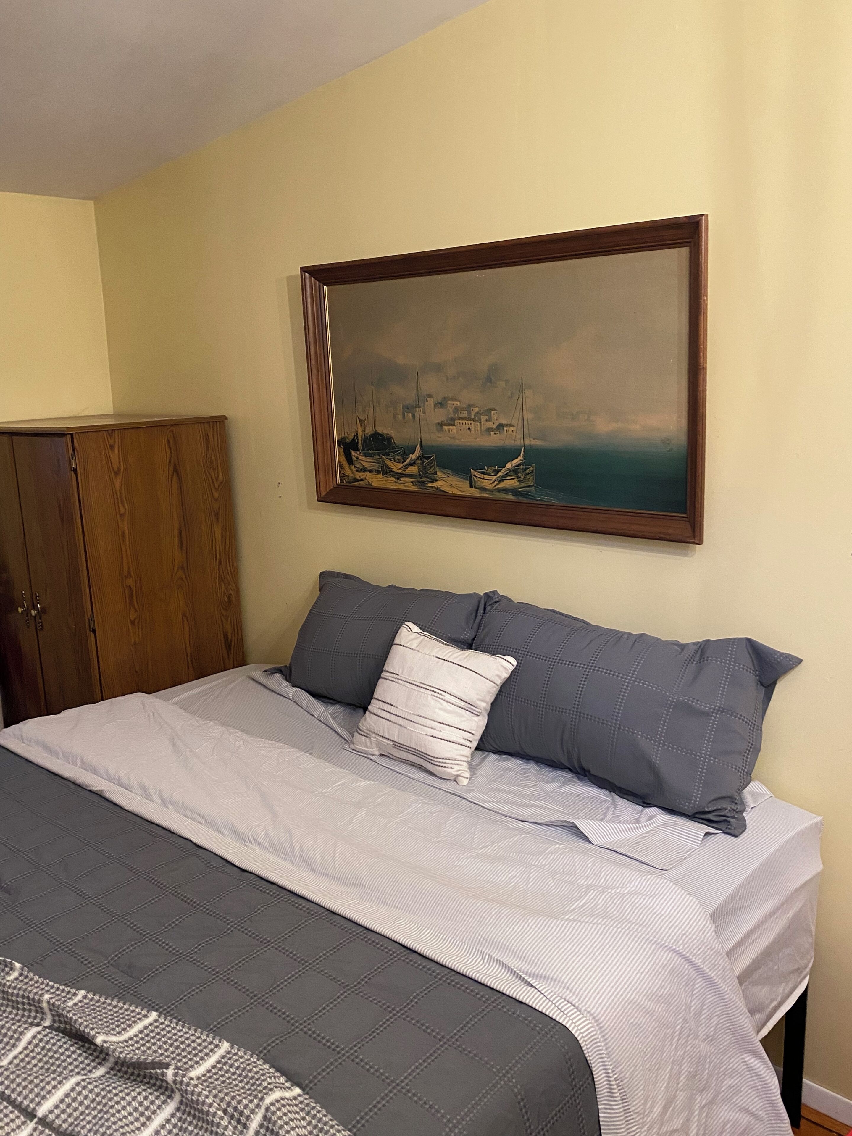 Quarto com cama, almofadas, um quadro e um guarda-roupa.