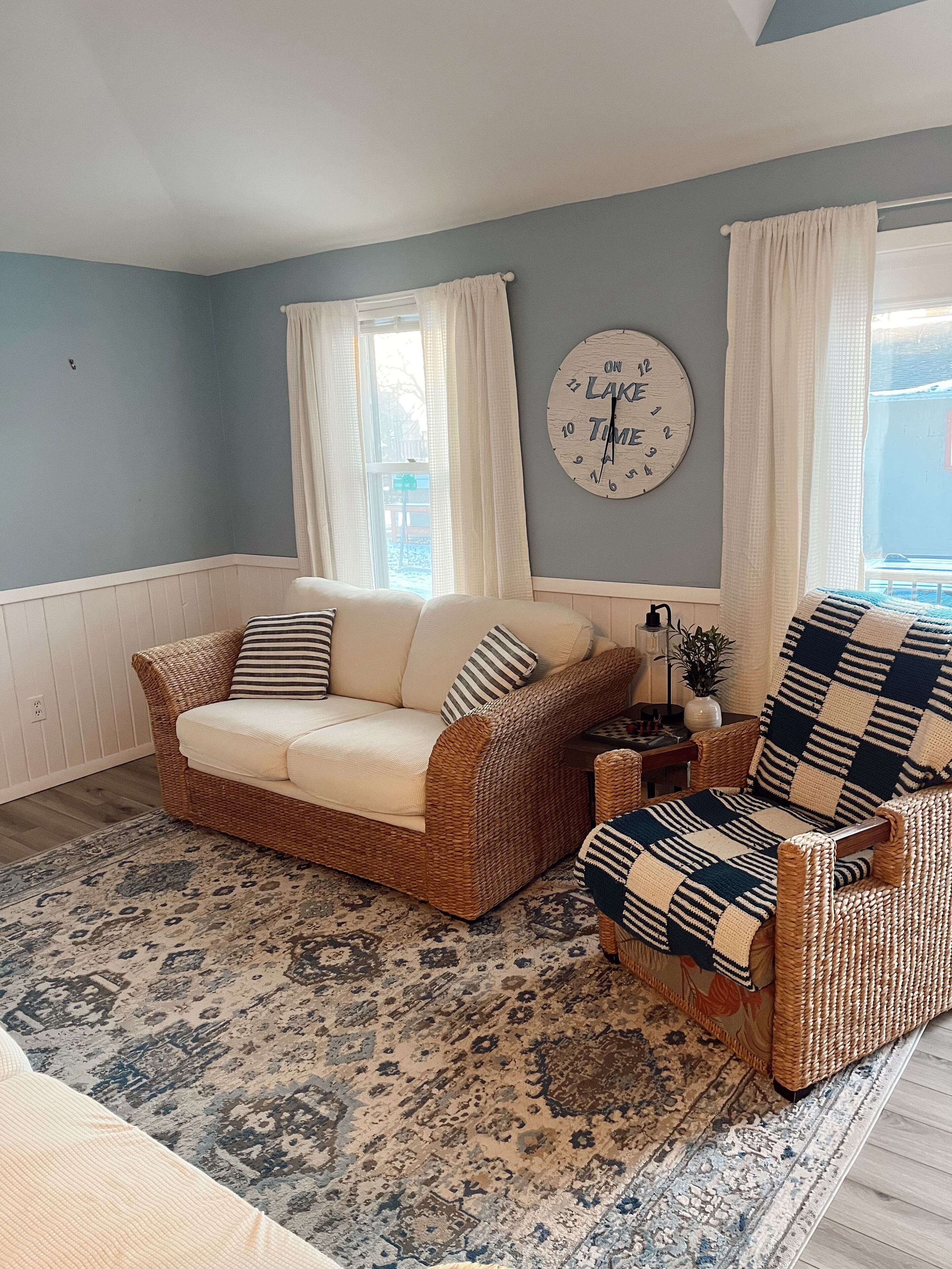 A living room with a wicker sofa, a patterned rug, and a wall clock.