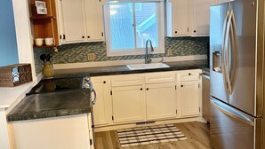 Une cuisine moderne avec des meubles blancs, un réfrigérateur en acier inoxydable, une fenêtre offrant une belle vue et un plancher en bois.