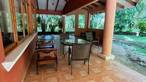 A covered patio with a tiled floor, wooden furniture, and large windows offering a view of a lush garden. - Congo House (Provincia de Guanacaste)