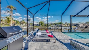A covered outdoor area with a grill, lounge chairs, and a pool. - Spacious 4-bedroom house in beautiful Cape Coral with WiFi, AC, Dock, Pool, Spa (Cape Coral)