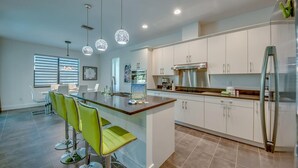 A modern kitchen with white cabinets, a stainless steel refrigerator, and a central island with bar stools. - Spacious 4-bedroom house in beautiful Cape Coral with WiFi, AC, Dock, Pool, Spa (Cape Coral)
