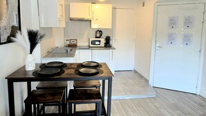 A compact kitchen with white cabinets, a microwave, and a coffee maker. There is a dining table with four stools. - L'Atelier-T2 near the Wifi-Parking center (Lourdes)