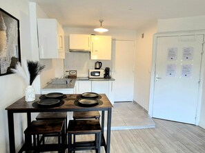 A compact kitchen with white cabinets, a microwave, and a coffee maker. There is a dining table with four stools. - L'Atelier-T2 near the Wifi-Parking center (Lourdes)