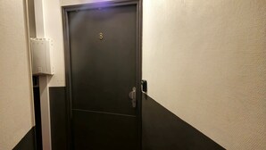 A narrow hallway with a dark-colored door, a wall-mounted intercom, and a textured wall. - L'Atelier-T2 near the Wifi-Parking center (Lourdes)