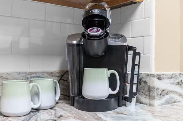 Una cafetera con dos tazas sobre una encimera de mármol.