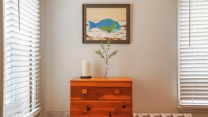 Una habitación con un aparador de madera, un cuadro de un pez enmarco, un jarrón con una planta y un radiador.