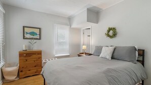 Un dormitorio con una cama grande, un aparador, un radiador, un cuadro en la pared y una puerta que da a otra habitación.