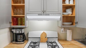 Cocina compacta con estufa a gas, cafetera y armarios con vasos y vajilla.