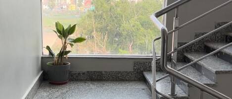 A staircase with granite steps leading to a landing, a potted plant on the landing, and a view of a cityscape through a large window.