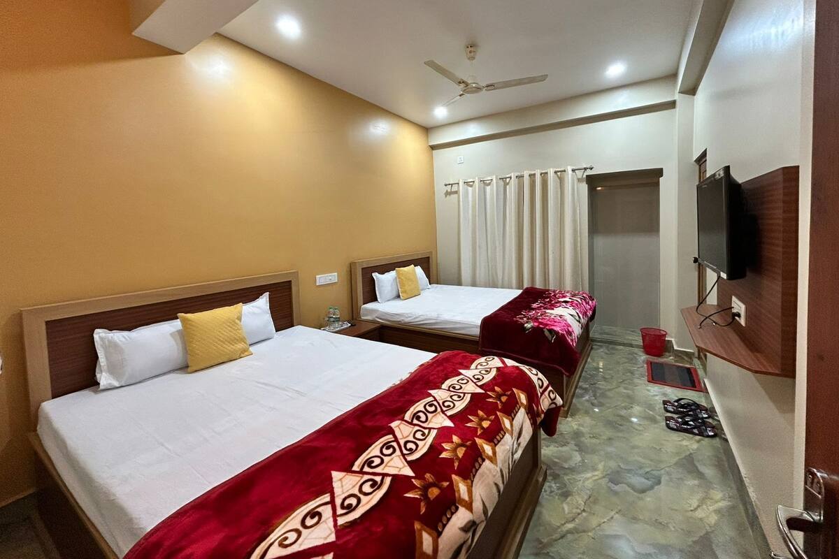 A hotel room with two beds, a ceiling fan, a television, and a bathroom door.