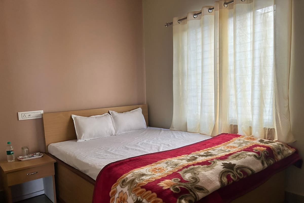 A bedroom with a bed, a nightstand, a power outlet, and a window with curtains.
