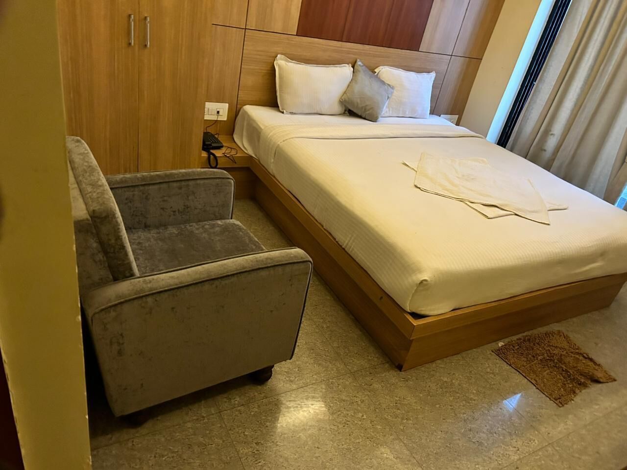 Ein Hotelzimmer mit einem Bett, einem Sessel, einem Holzschrank und einem kleinen Teppich.