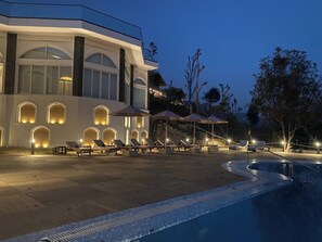 A modern hotel with a pool area, lounge chairs, and umbrellas.