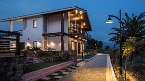 Een huis met twee verdiepingen, een balkon, stenen trappen en een pad dat naar de ingang leidt.