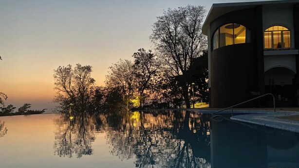 Een modern gebouw met een reflecterend zwembad, omringd door bomen en een zonsondergang.