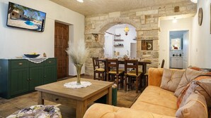 A cozy living room with a stone wall, wooden furniture, and a television mounted on the wall. - Holiday Home Marilu with pool (Stankovci)