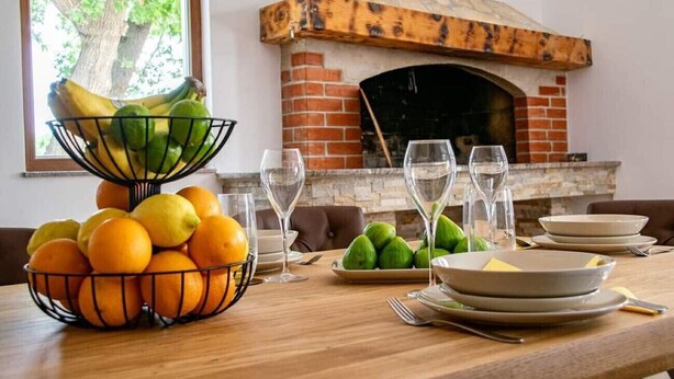 Una mesa de comedor con fruteros, copas de vino y platos, frente a una chimenea de ladrillo.