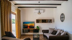 Una sala de estar con televisor, dos sofás, una mesa de centro y un ventanal con cortinas.