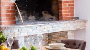 Una chimenea de ladrillo con detalles de piedra, una mesa de comedor con sillas y un frutero sobre la mesa.