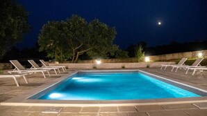Una piscina rectangular con borde de azulejos, rodeada de sillas de descanso y un muro de piedra.