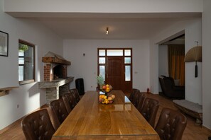 A spacious dining room with a long wooden table, leather chairs, a brick fireplace, and a large wooden door.