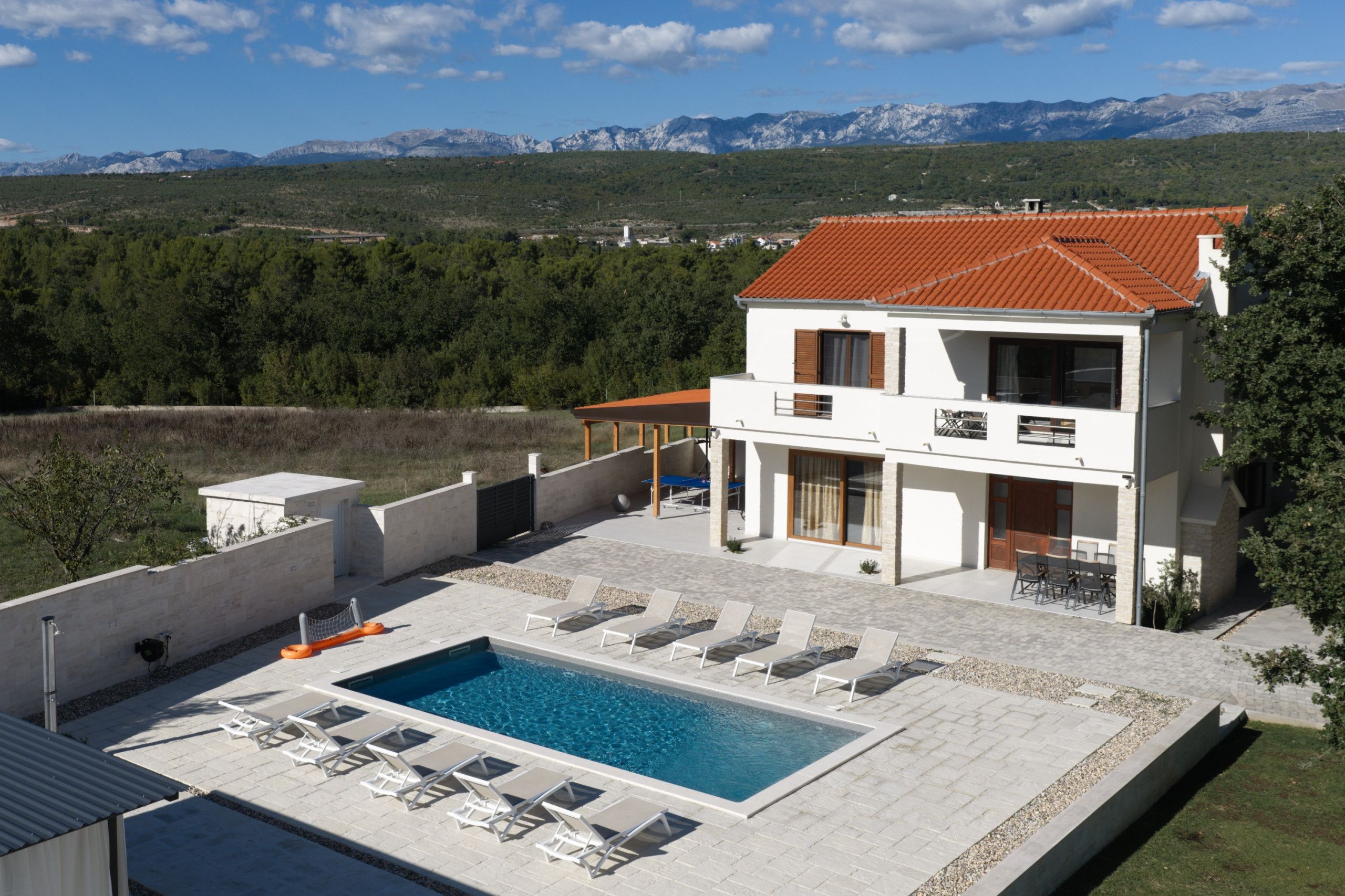 A two-story house with a swimming pool, outdoor seating, and a view of mountains.