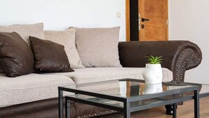 Una sala de estar moderna con una mesa de centro de vidrio, un sofá de cuero marrón y una maceta blanca con una planta.