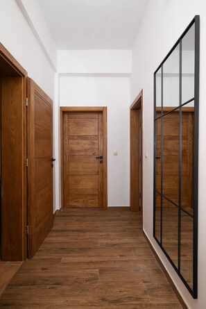 A hallway with wooden flooring, a central door, and a mirrored closet on the right.
