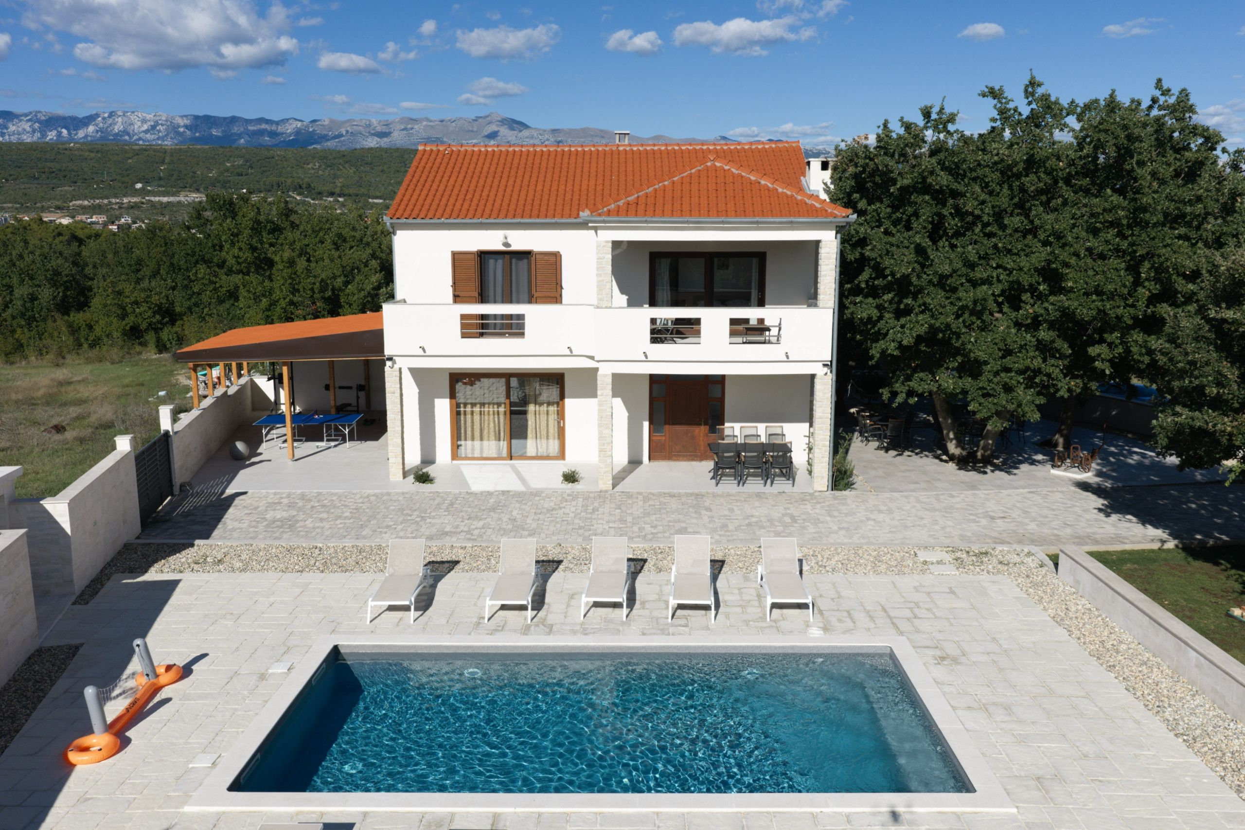 A two-story house with a swimming pool, outdoor seating, and a view of mountains.
