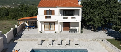 A two-story house with a swimming pool, outdoor seating, and a view of mountains.