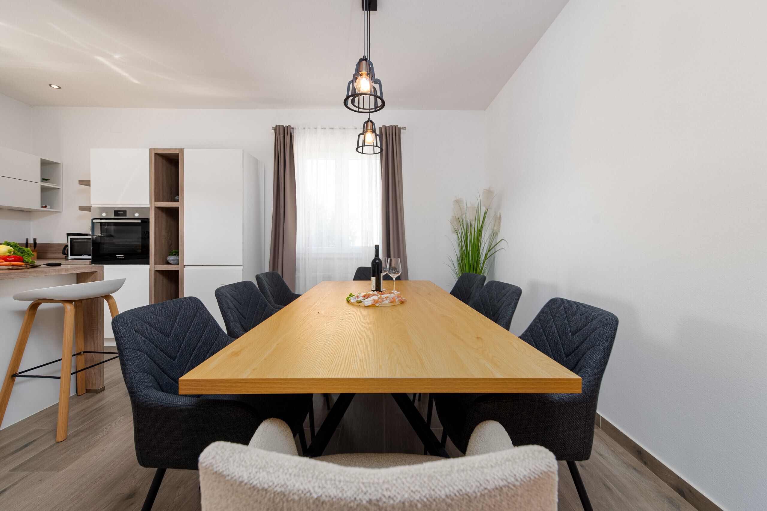 A modern dining area with a wooden table, six chairs, and a hanging light fixture.
