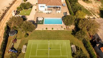 An aerial view of a residential property with a swimming pool, tennis court, and a fenced yard.