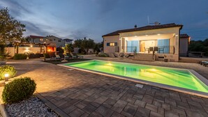 Une maison moderne dotée d’une piscine, d’un espace salon extérieur et d’une terrasse bien éclairée.