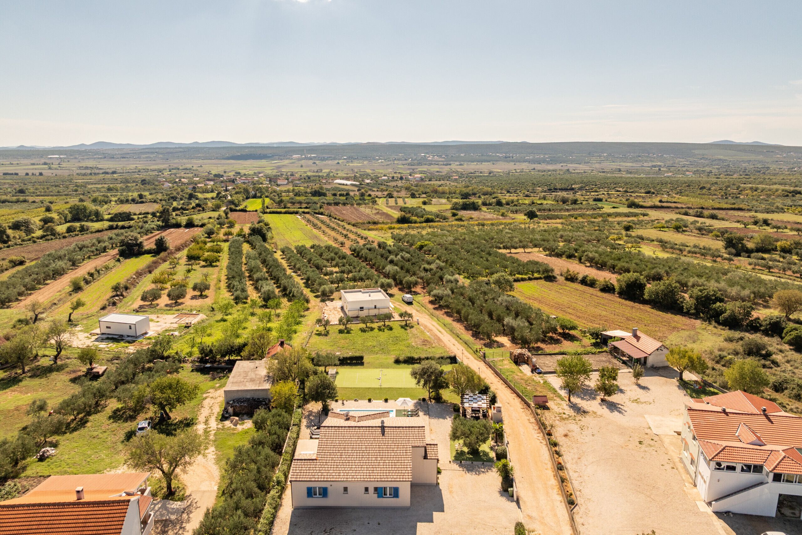 Vista aérea de una zona rural con campos, casas y una cancha de tenis.