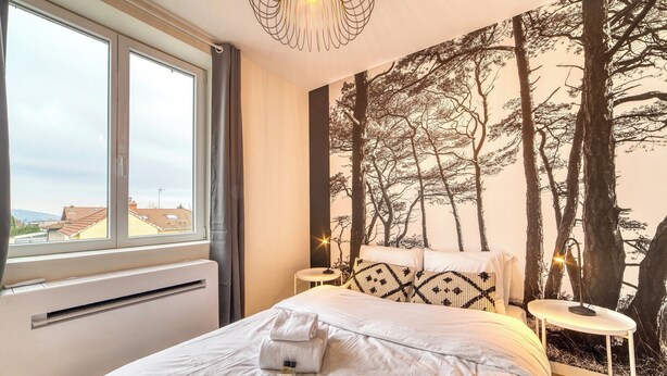 A bedroom with a large bed, a window, a wall mural, and a bedside table.