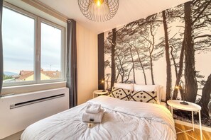 Une chambre avec un grand lit, une fenêtre, une fresque murale et une table de chevet.