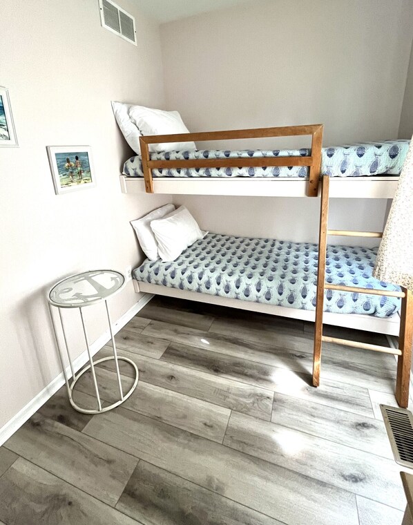 A bunk bed with patterned bedding, a small round table with an anchor design, and a radiator on the floor.