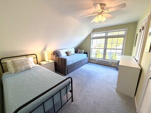 A bedroom with two beds, a ceiling fan, a window with blinds, and a radiator. - Endless Sunsets Main House (South Haven)