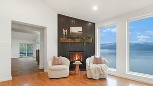 A spacious living room with a fireplace, two armchairs, and a large window overlooking a body of water. - Riverside Retreat  Sleeps 20 (Halifax)