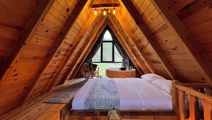 Ein gemütliches Schlafzimmer im Dachgeschoss mit schrägen Holzwänden, einem großen Fenster, einer runden Holzwanne und einem Bett mit weißen Leinentüchern.