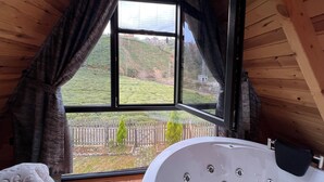 Ein Zimmer mit Holzboden, einem großen Fenster, einer Badewanne und Blick auf eine grüne Landschaft.