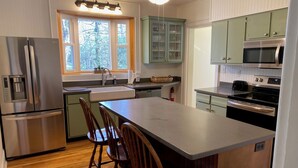 A kitchen with a central island, wooden chairs, stainless steel appliances, and light green cabinets.