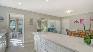 A modern kitchen with a large island, white cabinetry, and a view to a patio area.