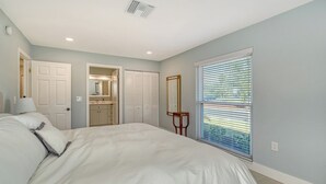A bedroom with a large bed, a walk-in closet, a bathroom, and a window with blinds.