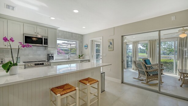 A modern kitchen with white cabinetry, a central island with stools, a microwave, and a toaster.