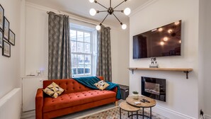 Een moderne woonkamer met een rode bank, behang met een patroon, een ronde salontafel en een open haard.